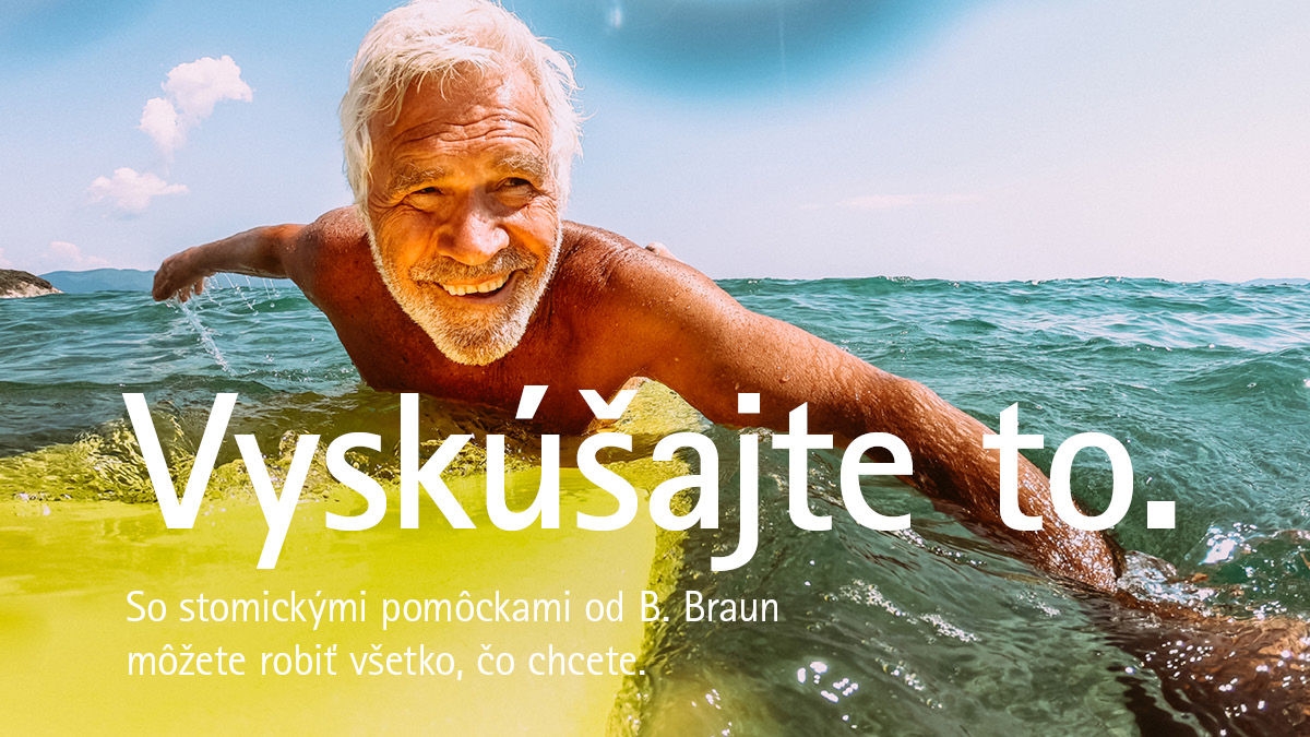 Starší muž s bielymi vlasmi leží na žltej surfovej doske a pádluje v oceáne pod čistou modrou oblohou.