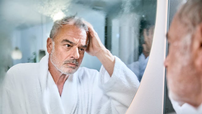 starší muž v župane sa premyslene pozerá do zahmleného zrkadla v kúpeľni