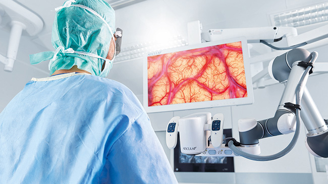 Chirurg vykonáva neurochirurgický zákrok s Aesculap Aeos®, pričom stojí vzpriamene a pozerá sa na monitor. 