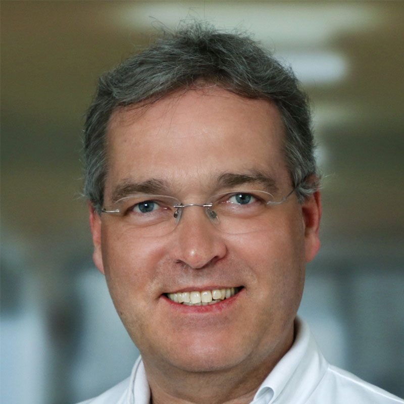 Portrét profesora Dr. Markusa Gollinga v doktorskom kabáte, ktorý sa sebavedome usmieva do kamery