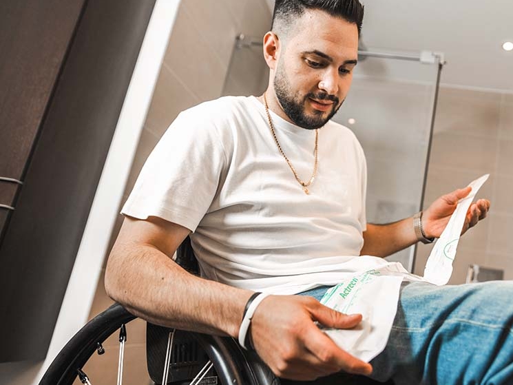 Muž na invalidnom vozíku, v pozadí kúpeľňa  , v ruke drží katéter  